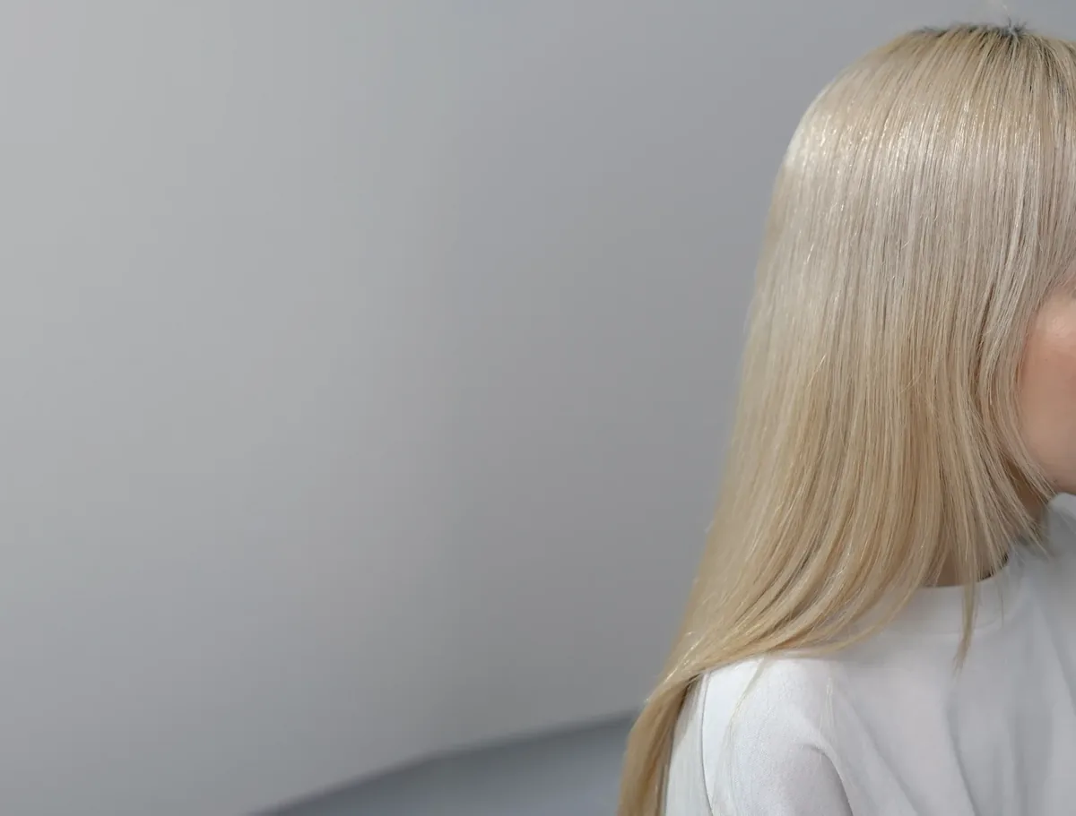 A model with long, smooth platinum hair against a grey studio backdrop
